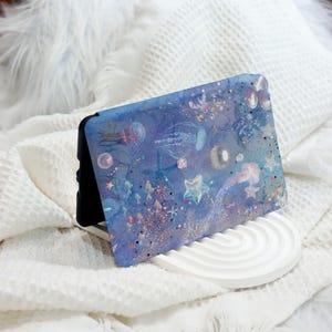 May include: A blue and purple phone case with a watercolour design of jellyfish, starfish, and other sea creatures. The case has a glittery finish.