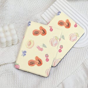May include: Two yellow e-reader covers with a fruit pattern. The pattern includes papaya, peaches, cherries, and blueberries. The covers are made of a soft, durable material and are designed to protect your e-reader from scratches and bumps.