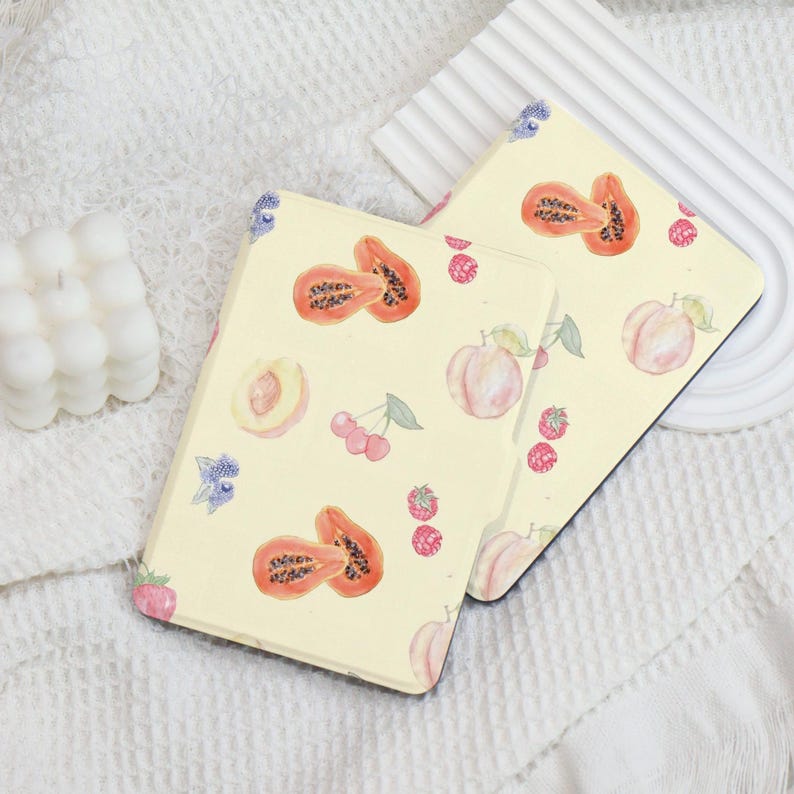 May include: Two yellow e-reader covers with a fruit pattern. The pattern includes papaya, peaches, cherries, and blueberries. The covers are made of a soft, durable material and are designed to protect your e-reader from scratches and bumps.