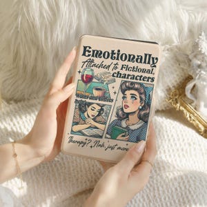 Op de afbeelding: Een beige e-reader hoes met een illustratie in stripstijl van een lezend persoon, met de tekst "Emotionally Attached to Fictional characters", "Wines and coffees help!" en "Therapy? Nah, just more books" in zwarte schreef- en scriptletters.