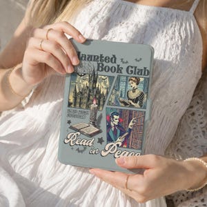 Op de afbeelding: Een lichtgrijze e-reader hoes met de tekst Haunted Book Club en Read in Peace. De afbeelding bevat een gotisch kasteel, een lezend persoon, een vampier in een bibliotheek, een brandende kaars, een open boek, vleermuizen en sterren in een vintage stijl.