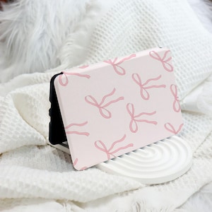 May include: A pink phone case with a repeating pattern of pink bows. The case is made of a soft, flexible material and has a black edge.
