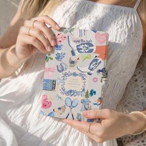 May include: A tablet case with a light grey background featuring a colourful pattern of cowboy boots, flowers, a chicken, tennis rackets, a mixer, and a horseshoe. The text reads "enjoy the ride" and "for we are god's masterpiece".