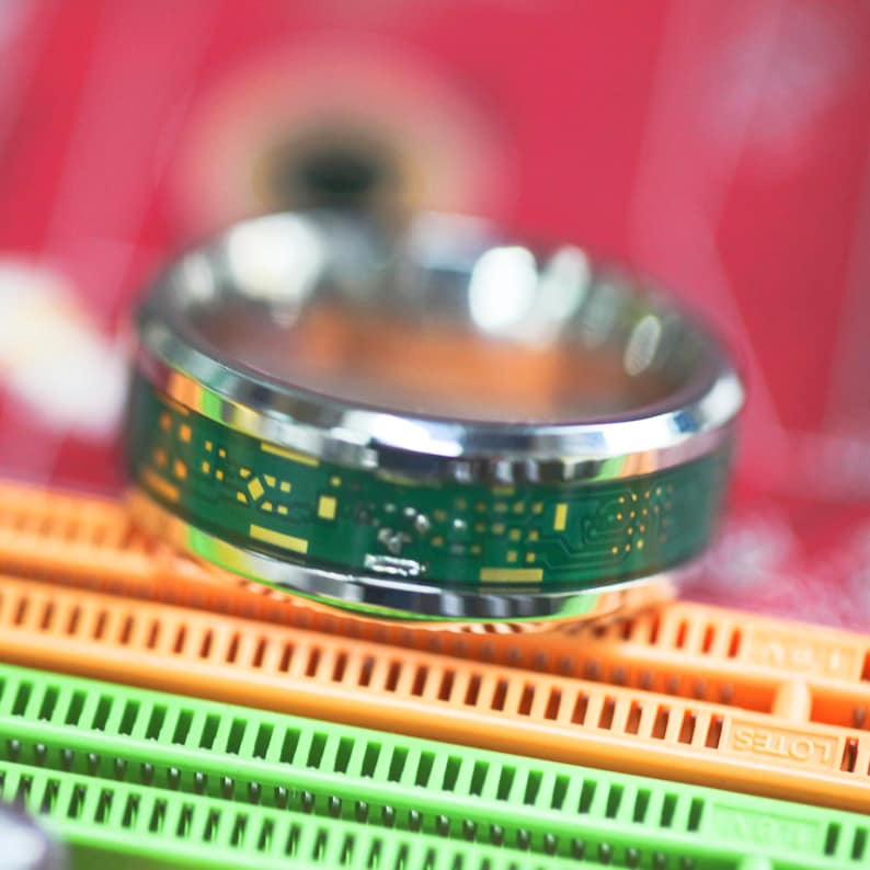 May include: A silver ring with a green circuit board design. The ring is on a red and orange background.