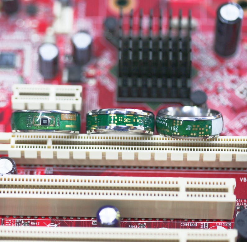 May include: Three silver rings with green circuit board designs. The rings are on a red and white background.