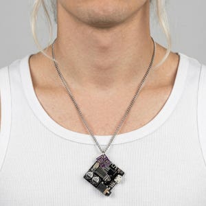 May include: A silver chain necklace with a pendant made from a black circuit board. The pendant has a square shape with a purple component at the top. The person is wearing a white tank top.
