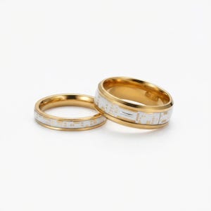 May include: Two gold-colored rings with a white band featuring a circuit board design. The rings are displayed on a white background. The rings have a polished finish and a modern aesthetic.