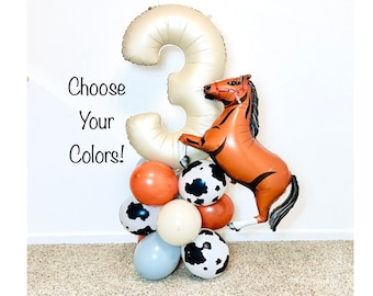 May include: A gold number three balloon with a brown horse balloon attached to it. The balloons are surrounded by smaller balloons in brown, white, black, and gray with a cow print pattern.