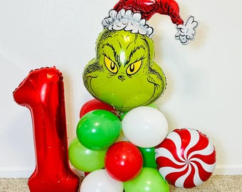 Pode incluir: Um arranjo festivo de balões com um grande número 1 vermelho, um balão verde em forma de Grinch usando um gorro de Papai Noel e um grupo de balões vermelhos, verdes e brancos. Um balão em espiral de hortelã-pimenta vermelho e branco adiciona um toque festivo.
