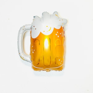 May include: A gold and white beer mug shaped foil balloon. The balloon is inflated and has a white foam top.