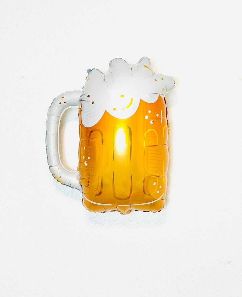May include: A gold and white beer mug shaped foil balloon. The balloon is inflated and has a white foam top.