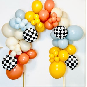 May include: A balloon arch made of white, blue, yellow, and red balloons. The balloons are arranged in a checkered pattern with black and white checkered balloons interspersed throughout the arch.