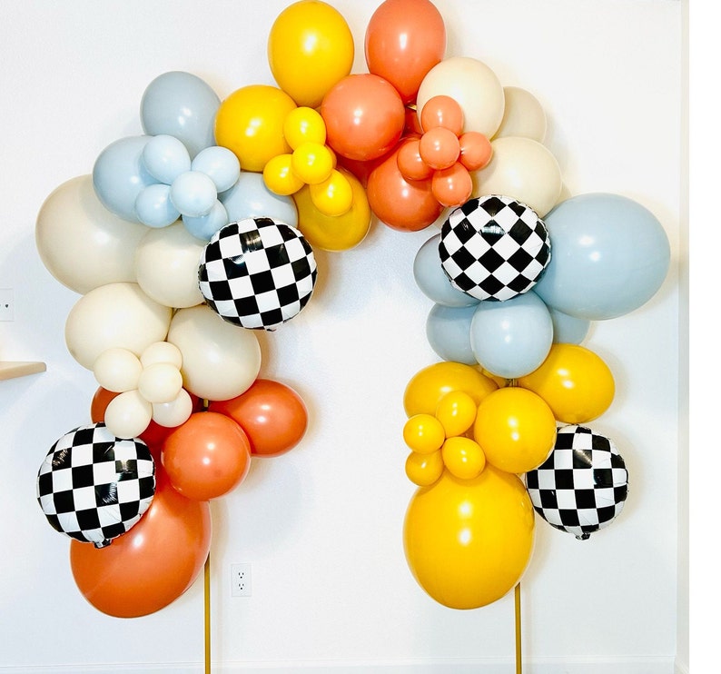 May include: A balloon arch made of white, blue, yellow, and red balloons. The balloons are arranged in a checkered pattern with black and white checkered balloons interspersed throughout the arch.