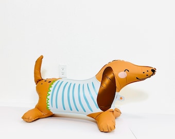 May include: A brown and orange dachshund balloon with a blue and white striped shirt. The balloon has a happy face and is perfect for a party or celebration.