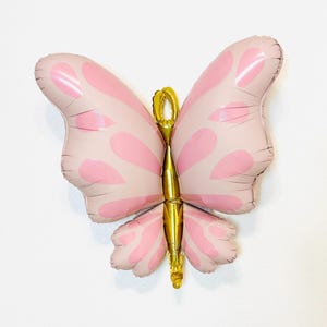 May include: A pink and gold butterfly shaped balloon. The balloon has a light pink color with darker pink spots and a gold body.