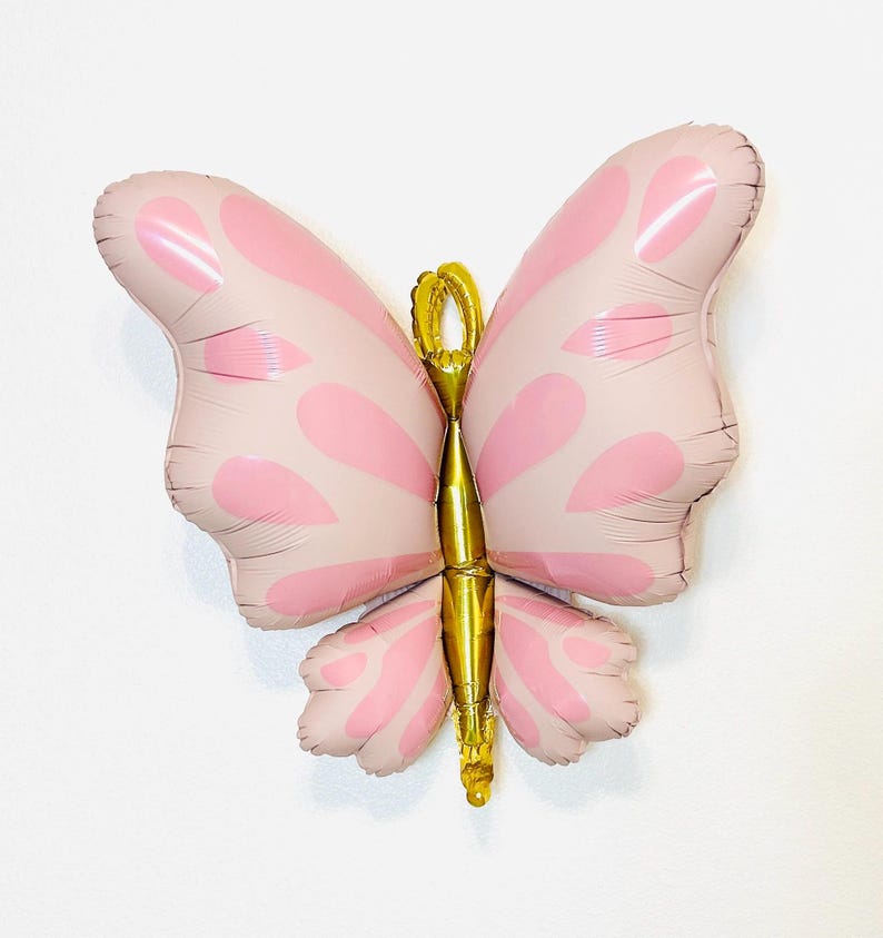 May include: A pink and gold butterfly shaped balloon. The balloon has a light pink color with darker pink spots and a gold body.