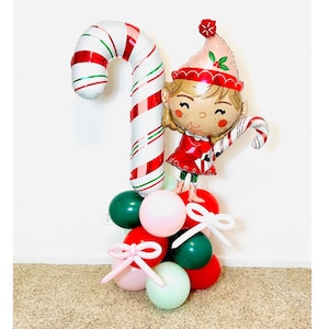 May include: A Christmas-themed balloon bouquet featuring a red and white candy cane balloon, a girl elf balloon holding a candy cane, and a cluster of red, green, pink, and white balloons.
