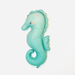 May include: A teal blue seahorse shaped balloon with a glittery finish. The balloon has a cute face with closed eyes and a small mouth.