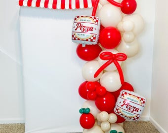 May include: A festive balloon arch featuring red, white, and cream-colored balloons. The arch includes red bows, balloon "tomatoes" with green leaves, and two square balloons with "Pizza+" text. A red and white striped awning tops the display.