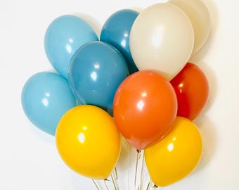 Può includere: Un mazzo di palloncini blu, gialli, arancioni e crema. I palloncini sono legati insieme con uno spago dorato.