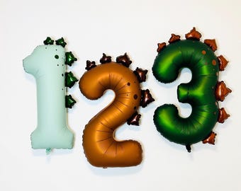 May include: Three foil balloons shaped as the numbers one, two, and three. The number one is light mint green with dark green spikes. The number two is copper with dark brown spikes. The number three is dark green with copper spikes.