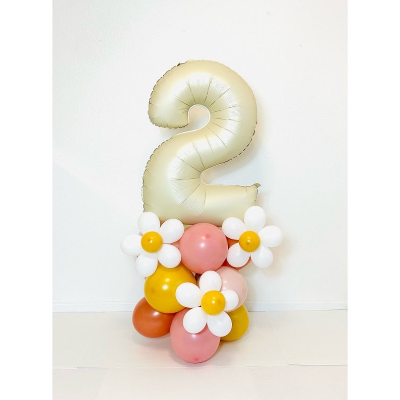 Puede incluir: Un globo de n&uacute;mero dos dorado con un grupo de globos rosas, amarillos y blancos debajo. Los globos blancos tienen un dise&ntilde;o de margarita.