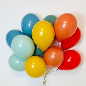 May include: A cluster of colorful balloons in shades of blue, green, yellow, orange, and red. The balloons are tied together with gold string, creating a festive and celebratory arrangement. Perfect for birthdays, parties, or any special occasion.