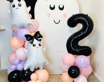 May include: A balloon display featuring a large white ghost backdrop with a black bow, two smaller ghost-shaped foil balloons with black bows, and a large black foil balloon in the shape of the number two, accented by pink, purple, and black balloons.