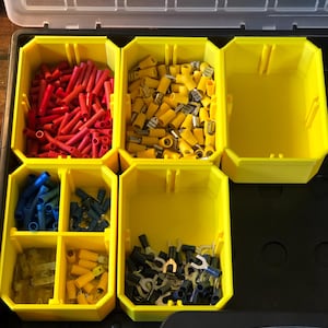 May include: A yellow plastic organizer filled with various electrical connectors. The compartments hold red, yellow, blue, and black crimp terminals and wire ferrules. The organizer is open, revealing the contents.