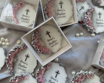 May include: A collection of white round favors with pink and silver glitter accents. Each favor features a cross and the text "Amira's Baptism 16.03.2025".