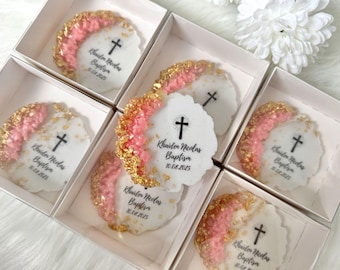 May include: White, scalloped-edge favors with pink and gold accents, each featuring a cross and the text "Khuiden Nicolas Baptiza 10.08.2025". The favors are presented in individual white boxes, ideal for a baptism.