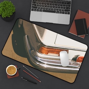 May include: A rectangular mouse pad featuring a vintage car design. The image shows the rear of a classic white car with chrome detailing and orange taillights. A white computer mouse sits on the pad, alongside a laptop, notebooks, and a cup of coffee.