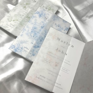 May include: A set of wedding invitations with a floral design. The invitations are printed on white paper with a light blue floral pattern. The text on the invitations is in black ink. The invitations are folded in half and have a white envelope.