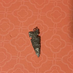 May include: A silver arrowhead pendant with a textured surface.