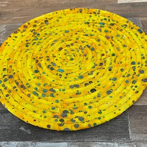 May include: A yellow round crocheted coaster with a circular pattern of dark blue and green dots.