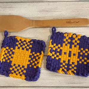 May include: Two purple and gold woven pot holders. The pot holders are square and have a checkered pattern.