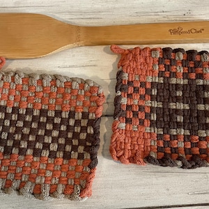 May include: Two brown and orange woven pot holders with a wooden spatula with the text "Pampered Chef" on it.