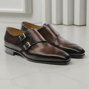 Pode incluir: Um par de sapatos castanhos de couro com fivela dupla. Os sapatos têm um acabamento polido, fivelas prateadas e um design de biqueira. Os sapatos são exibidos em uma superfície branca.