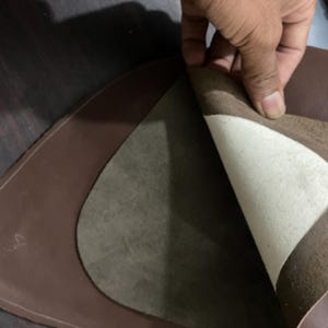 May include: A close-up of brown leather pieces, one layer peeled back to reveal a lighter, textured interior. The edges are neatly stitched, suggesting a craft or leatherwork project. The image highlights the material's texture and color variations.