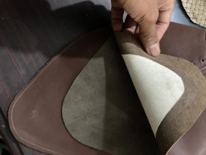 May include: A close-up of brown leather pieces, one layer peeled back to reveal a lighter, textured interior. The edges are neatly stitched, suggesting a craft or leatherwork project. The image highlights the material's texture and color variations.