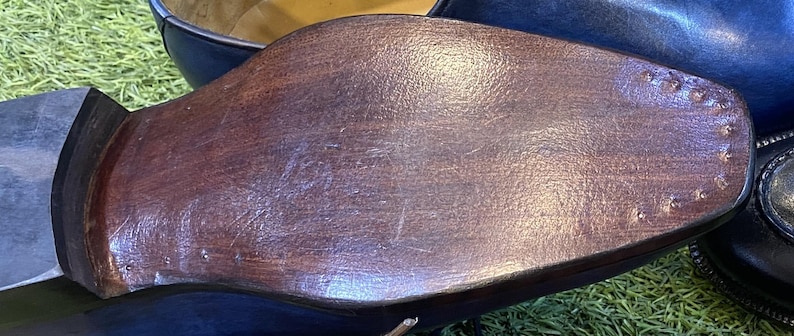 May include: Close-up of the sole of a dark brown leather shoe. The sole is worn and shows signs of use. The shoe is part of a collection of blue leather shoes, with a glimpse of the upper visible.