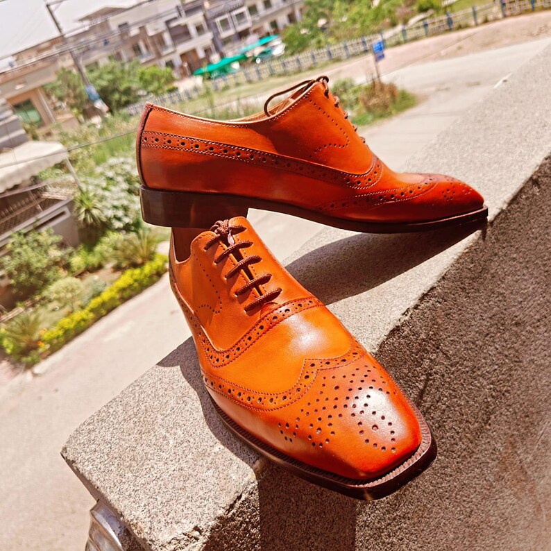 May include: A pair of brown leather Oxford shoes with decorative perforations and a lace-up closure. The shoes have a classic wingtip design and a polished finish, perfect for formal or business attire.