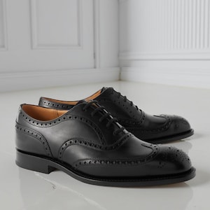 May include: A pair of black leather Oxford shoes with brogue detailing. The shoes feature a classic wingtip design with decorative perforations along the seams and toe cap. The shoes have black laces and a low heel.