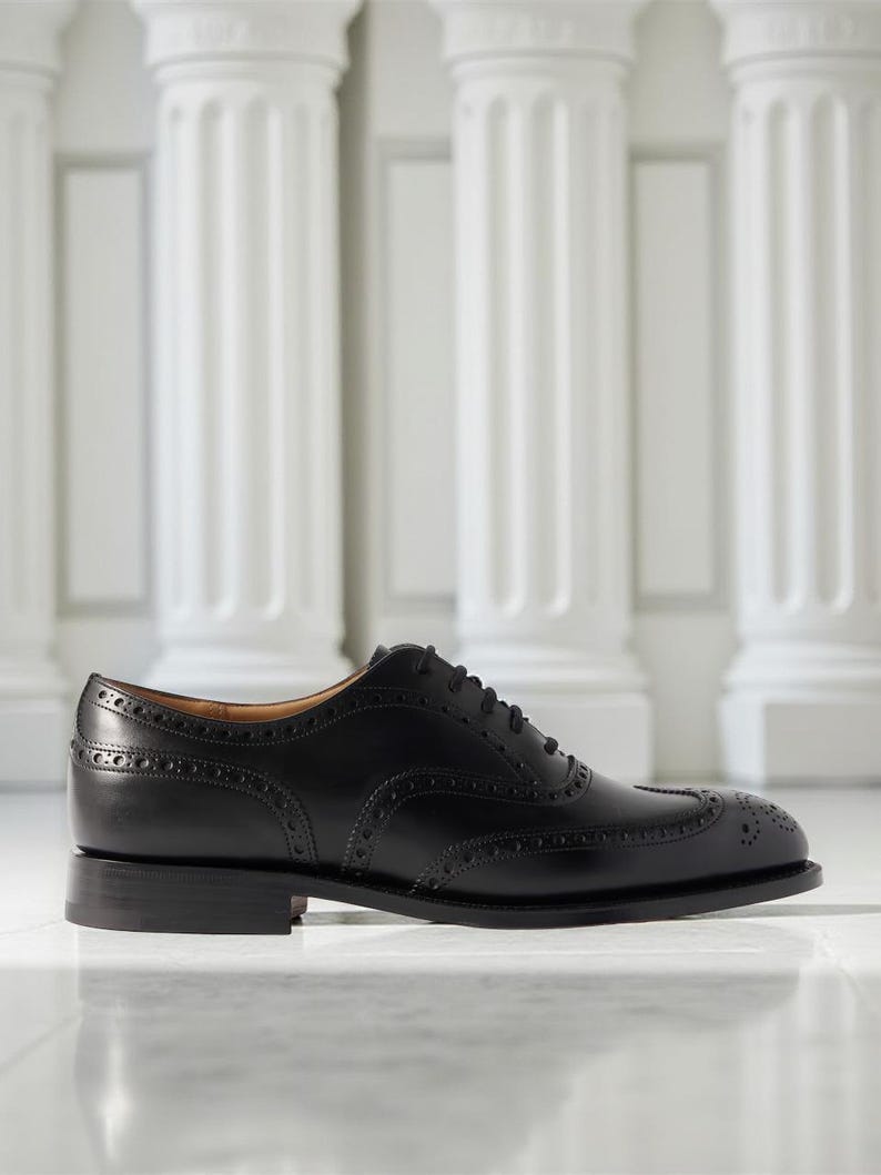 May include: A black leather Oxford shoe with brogue detailing. The shoe features a classic wingtip design and a low heel. The shoe is displayed on a reflective surface with white columns in the background.