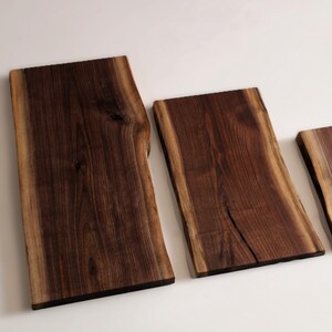 Peut inclure: Trois planches de service en bois avec des bords naturels. Les planches sont en bois brun foncé avec des bords brun clair. Les planches sont rectangulaires, la plus grande à gauche et la plus petite à droite.