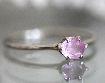May include: A delicate silver ring with a pale pink oval gemstone set in a prong setting.