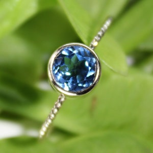 May include: A delicate silver ring with a round blue topaz gemstone.