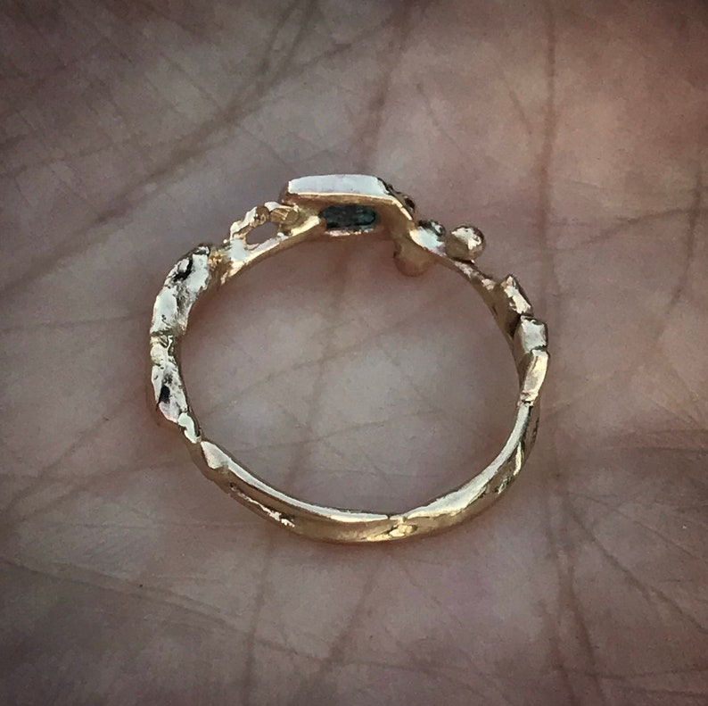 May include: A gold ring with a textured band and a small, dark blue stone set in the center.