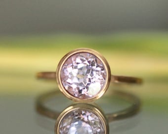 May include: A delicate gold ring with a bezel setting featuring a pale pink oval gemstone.
