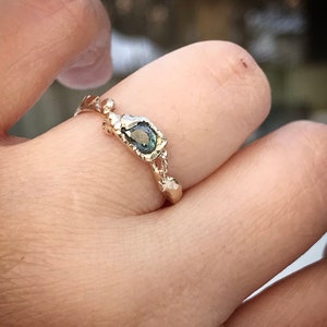May include: A gold ring with a green gemstone set in a textured band. The ring is on a person's finger.